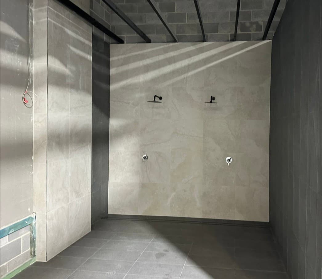 Shower plumbing roughed in ahead of tiling, with matte black valves on a bathroom wall