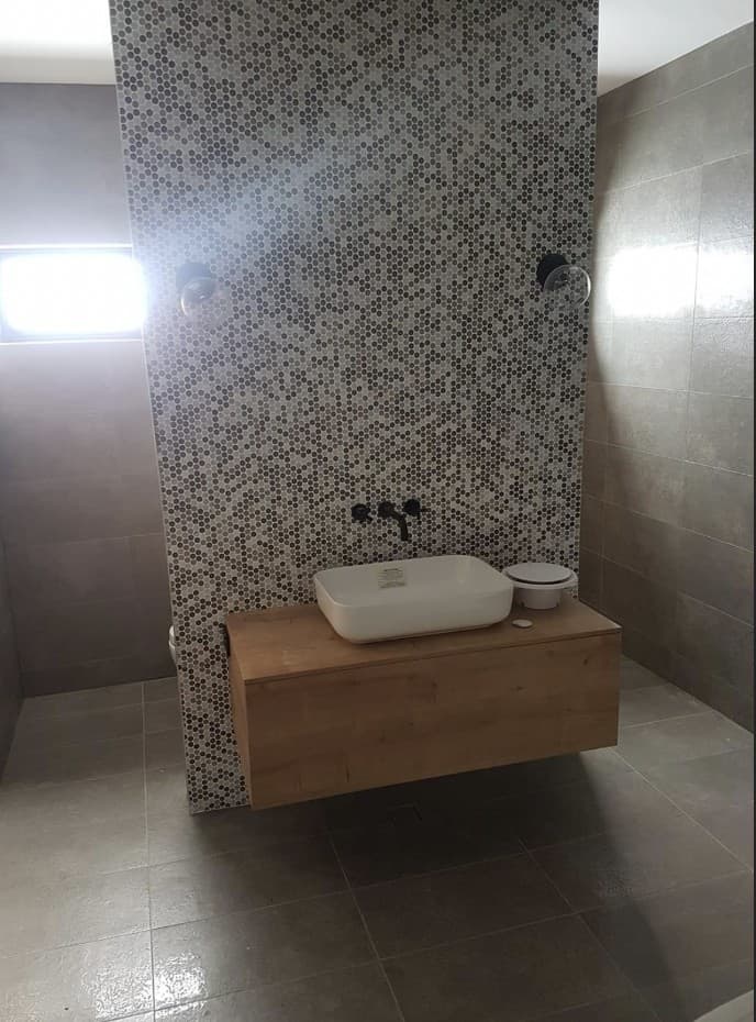 Floating timber vanity with vessel sink and black tapware against a mosaic tile feature wall
