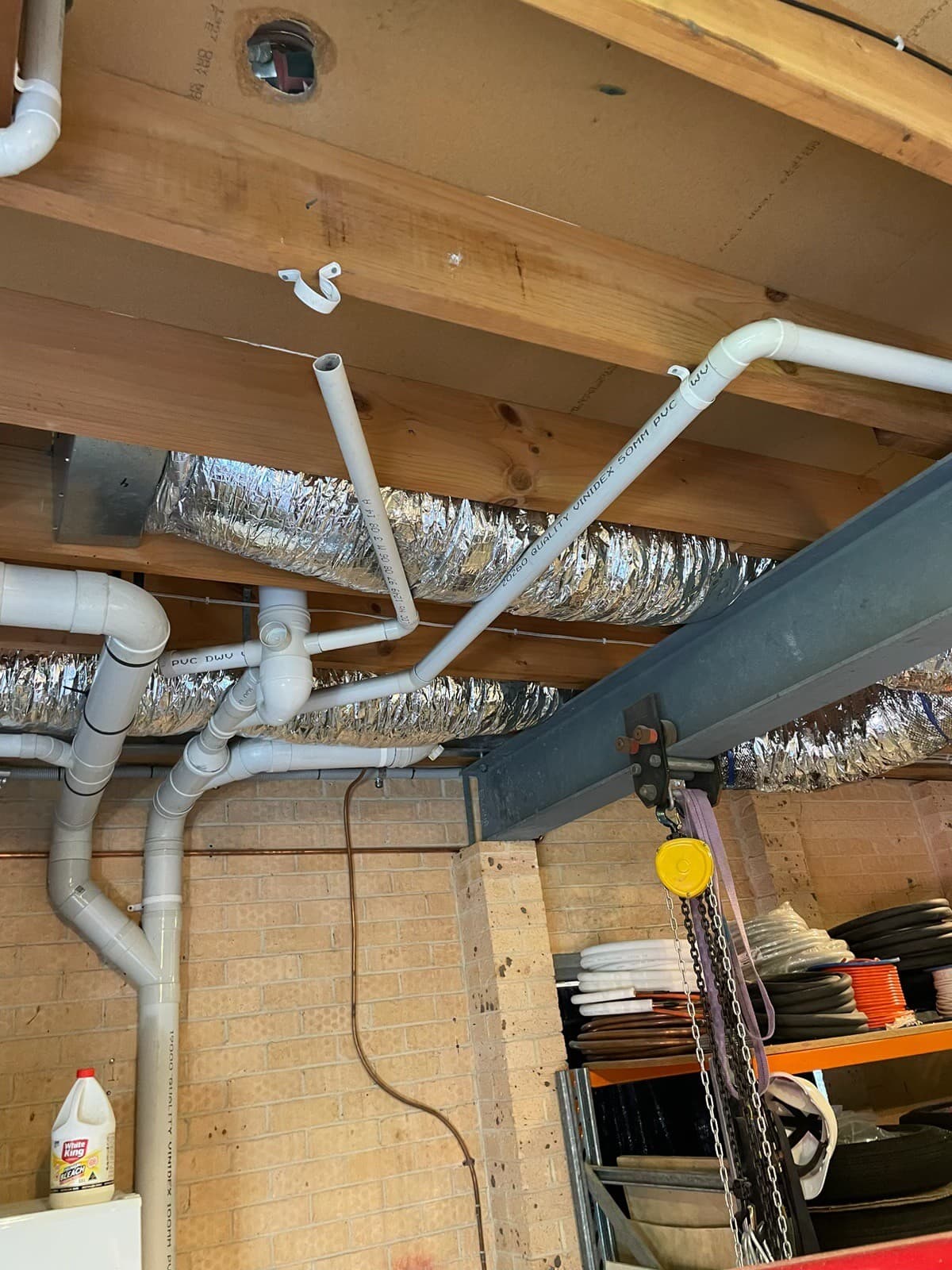 PVC drainage pipework and ducting run through subfloor joists during a renovation